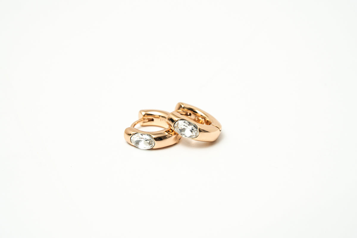 Pair of rose gold hoop earrings with clear gemstones on a white background